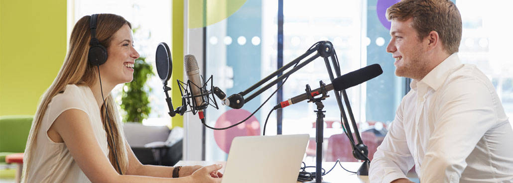 Two people at microphones and a laptop