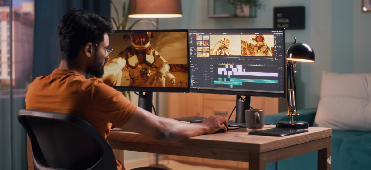 Man editing video sitting in front of two computer screens and a laptop