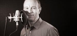 Man recording on a microphone in a black area.