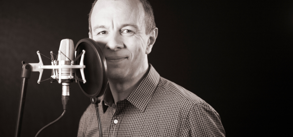 Man recording on a microphone in a black area.